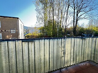 Balkon s dlažbou a výhledem na vzrostlé stromy, ideální pro relaxaci. Tepelná izolace zajišťuje příjemné klima v moderním prostředí.