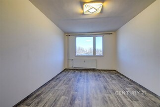 Prázdná světlá místnost s moderní plovoucí podlahou, velkými okny a bílými stěnami, ideální pro vytvoření útulného obytného prostoru.