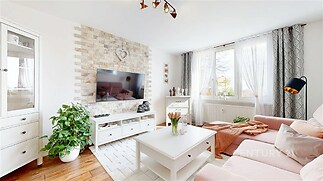 Světlý obývací pokoj s parketovou podlahou, velkými okny a moderním dekorativním kamenem na stěně, poskytující útulnou atmosféru.