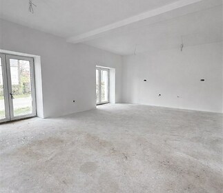 Prázdný obývací pokoj s velkými okny a bílými stěnami, připravený k dokončení, moderní prostor vhodný pro úpravy podle vlastního vkusu.