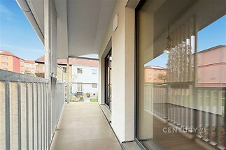 Balkon s hladkou dlažbou a moderním zábradlím, výhled do klidného dvora, velká okna zajišťující světlost interiéru.