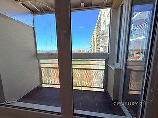 Balkon s dlažbou, moderní zasklení a výhledem na městskou architekturu. Prostorný a praktický pro relaxaci.