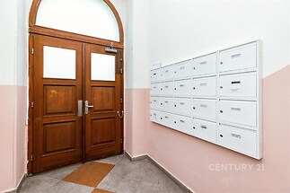 Vstupní chodba s dřevěnými dveřmi, dlažbou a poštovními schránkami. Světlý prostor v bytovém domě.