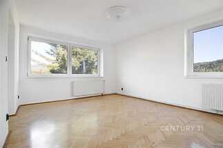 Světlý obývací pokoj s parketovou podlahou a velkými okny, moderní a dobře osvětlený prostor vhodný pro rodinné bydlení.