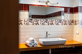 Moderní koupelna s keramickými obklady, dřevěnou deskou a velkým zrcadlem, nabízí elegantní a stylový prostor.