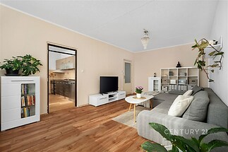 Světlý obývací pokoj, parketová podlaha, moderní nábytek, velká okna propojující prostor s kuchyní, světlé zdi dodávají vzdušnost.