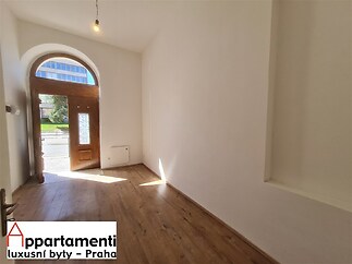 Vstupní hala s parketovou podlahou a dřevěnými dveřmi, nabízí vysoké stropy a světlý prostor, ideální pro moderní renovaci.