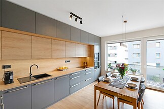 Moderní kuchyň s parketovou podlahou, velká okna pro přirozené světlo, elegantní vestavěné skříně a stylový jídelní stůl, ideální pro rodinné večeře