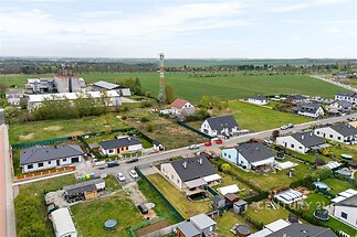 Letecký pohled na obytnou čtvrť s rodinnými domy, zahradami a sousedící zemědělskou krajinou, moderní architektura a klidné prostředí.