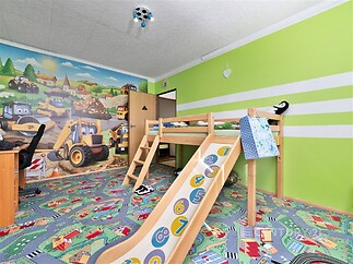 Dětský pokoj s veselou tapetou, herní skluzavkou a barevným kobercem, ideální pro rodiny, moderní design a světlé barvy zvýrazňují prostor.