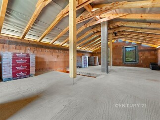Prostorná podkrovní konstrukce s dřevěnými trámy, betonová podlaha, velké okno s výhledem, příprava pro dokončení, moderní stavba.