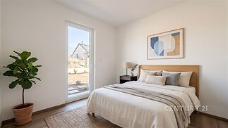 Světlá ložnice s moderním stylem, dřevěnou podlahou a velkým oknem. Obsahuje elegantní dekorace a pokojovou rostlinu, nabízí útulný a vzdušný prostor.