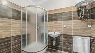 Moderní koupelna s keramickou dlažbou a obklady, sprchový kout, elektrický bojler, světlé odstíny hnědé, dobře udržovaná.