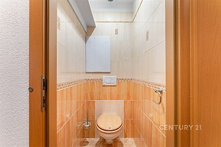 Malá koupelna s dřevěným obložením, moderní dlažbou a světlými obklady, vybavená toaletou a držákem na toaletní papír.