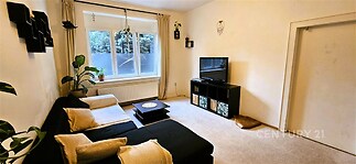 Světlý obývací pokoj s velkými okny, černobílou sedací soupravou a moderním kobercem, ideální pro rodinné bydlení.