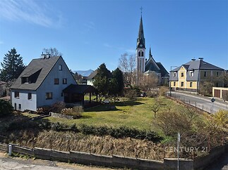 Prázdná zahrada před rodinným domem, s travnatou plochou a výhledem na venkovský kostel. Nachází se v klidné lokalitě.