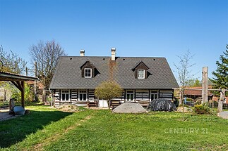 Tradiční venkovský dům s dřevěnou konstrukcí a šindelovou střechou, obklopený zelenou zahradou. Rustikální design a klidné okolí.