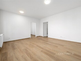 Světlý obývací pokoj s parketovou podlahou a moderním designem, propojený s dalšími místnostmi, vytváří pocit prostornosti a vzdušnosti.