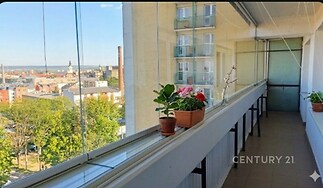 Zasklená lodžie s keramickou dlažbou a výhledem na město, ideální pro relaxaci a pěstování rostlin, nabízí klidné útočiště ve vyšším patře budovy.