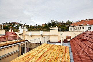 Střešní terasa s dřevěnou podlahou nabízí výhled na historické budovy, vhodná pro relaxaci, klidné prostředí v centru města.