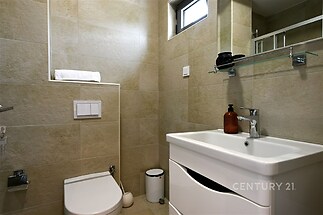 Koupelna s moderními dlaždicemi, elegantní umyvadlo a zrcadlo. Kompaktní prostor s úložnými možnostmi, čisté linie a světlé barvy.