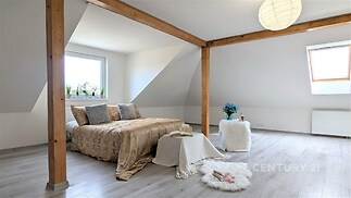 Prostorná ložnice s parketovou podlahou, moderní dřevěné trámy, světlá místnost s velkým oknem a střešním oknem pro přirozené světlo.