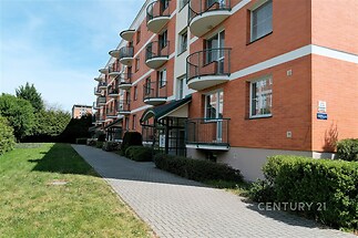 Červená cihlová fasáda moderního bytového domu s balkonem a zámkovou dlažbou, udržovaný trávník a zahrada, klidná lokalita.