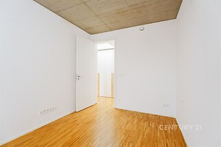 Prázdná ložnice s parketovou podlahou, bílými stěnami a betonovým stropem, moderní a minimalistický design, připravená k nastěhování.