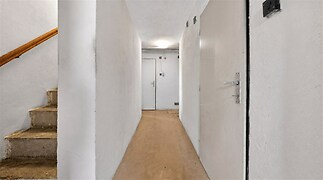 Úzká chodba s bílými stěnami a dřevěným schodištěm, původní stav, vhodná k rekonstrukci