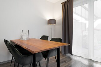 Jídelna s dřevěným stolem, moderními židlemi a velkými okny, parketová podlaha, elegantní styl, světlé prostory.
