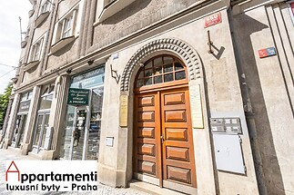 Vchod do historické budovy s dřevěnými dveřmi a zdobeným obloukem, zachovalá fasáda, ulice s dlažbou, komerční prostor ve spodním patře