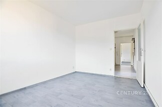 Světlý pokoj s moderní parketovou podlahou, bílé stěny a dveře vedoucí do chodby, ideální pro snadnou personalizaci interiéru.