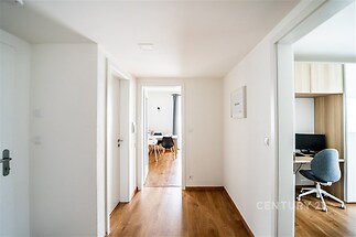 Světlá chodba s parketovou podlahou, moderní dveře vedou do pokojů, vestavěná pracovní plocha vpravo, čisté bílé stěny