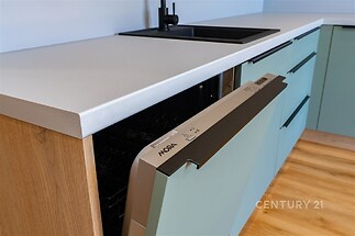Moderní kuchyň s vestavěnou myčkou, dřevěná podlaha, minimalistické úchyty, světlé povrchy, elegantní dřez s černou baterií