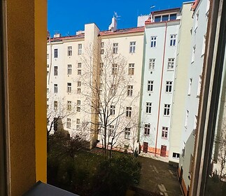 Pohled z okna na vnitroblok, který nabízí klidné prostředí. Vysoká činžovní budova s historickými detaily tvoří urbanistickou scenérii.
