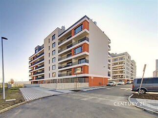 Moderní bytový dům s velkými okny a balkony, novostavba s moderní fasádou a parkovacím zázemím, vhodný pro rodinné bydlení.