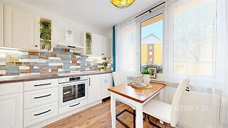 Světlá kuchyň s parketovou podlahou, velká okna, moderní vybavení, dřevěný stůl, dlaždicová zástěna, útulný styl.