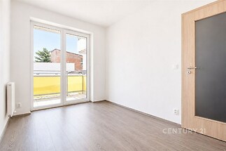 Světlá ložnice s parketovou podlahou, velká okna vedoucí na balkon, moderní interiér v neutrálních tónech.
