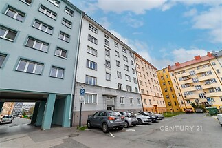 Pohled na bytový dům s parkovištěm, rekonstruovaná fasáda, plastová okna, venkovní parkovací místa, klidná lokalita městské části.