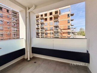 Moderní balkon s dlažbou, výhled na rozestavěný bytový komplex, čisté linie a dostatek prostoru pro relaxaci.