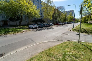 Ozeleněné okolí bytového domu s parkovacími místy na ulici, vhodné pro rezidentní bydlení.