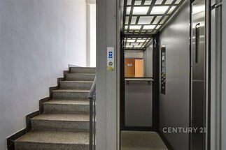 Vstupní prostor s moderním výtahem a kamennými schody, ideální pro rekonstruovaný bytový dům s dobrou dostupností a bezpečnostními prvky.