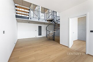 Moderní obývací prostor s parketovou podlahou, otevřeným schodištěm a vysokými stropy, který dodává prostoru světlo a vzdušnost.