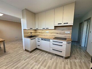 Moderní kuchyň s dřevěnými pracovními deskami a světlou parketovou podlahou, vybavená vestavěnými skříněmi v neutrálních tónech.