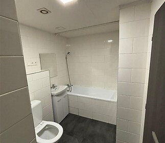 Koupelna s dlažbou, bílými obklady a vanou, vybavená moderním sanitárním zařízením, ideální pro rekonstruovaný byt.