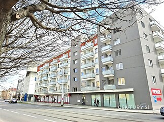 Šestipodlažní bytový dům s moderní fasádou, balkony a komerčními prostory v přízemí, ideální lokace v centru města.
