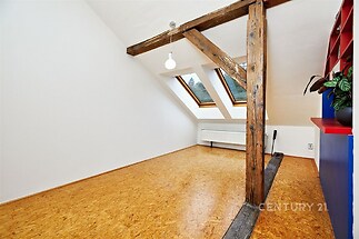 Podkrovní pokoj s parketovou podlahou, dřevěnými trámy a velkými střešními okny, které poskytují dostatek přirozeného světla.