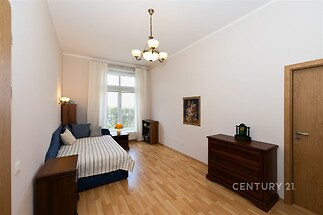 Světlá ložnice s parketovou podlahou, velkým oknem a dřevěným nábytkem, která poskytuje elegantní a útulný prostor.