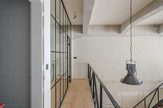 Moderní chodba s parketovou podlahou, prosklenými stěnami a kovovým zábradlím nabízí industriální styl a světlé prostory.