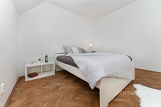 Prostorná ložnice, parketová podlaha, moderní nábytek, světlé stěny, útulná atmosféra, minimalistický design.